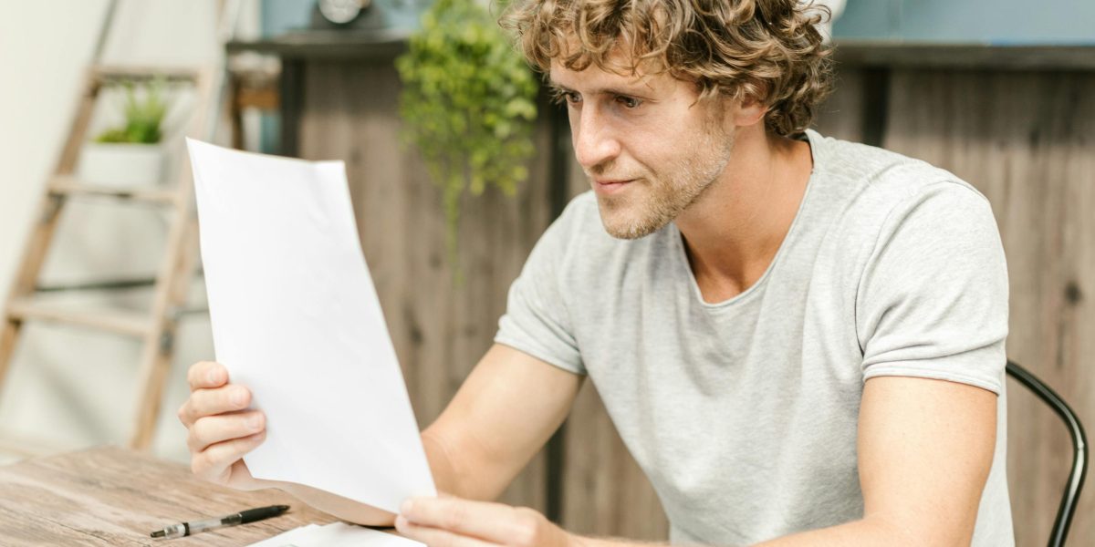 A person thoughtfully reviewing documents at a coffee shop, representing the careful budgeting needed for rental costs.